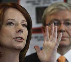 Julia Gillard speaks with her hand held up, Kevin Rudd's face is in the background
