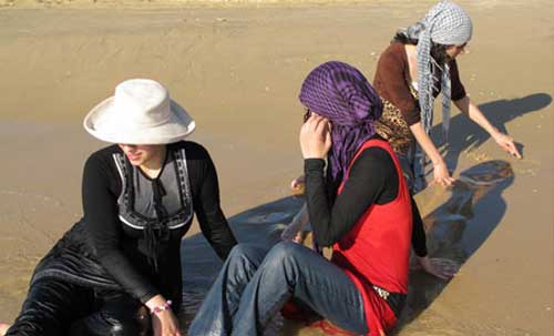 3 women sit in very shallow waves at the edge of the sea