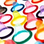 An assortment of condoms in rainbow colours arranged on a flat surface photographed on a tilt