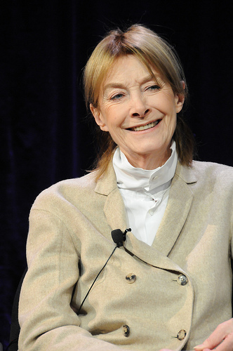 a pale skinned smartly dressed elderly woman is wearing a lapel mic for an interview and smiling