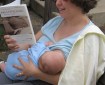 A pale skinned woman reads 'Breastfeeding: A Parent's Guide' while nursing a baby