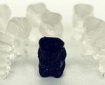a lone black gummy bear is surrounded by white gummy bears - they are posed as if ganging up on the black gummi bear