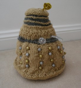 A gold Dalek with silver accents and gold and silver beads as its bobbles. The plunger and ray gun are made of a silver pipecleaner, and the eyestalk out of a gold one.