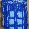 A knitted toy TARDIS, in dark blue with light blue detailing and white lettering.