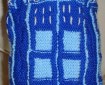 A knitted toy TARDIS, in dark blue with light blue detailing and white lettering.