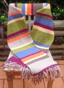 A long and while multicoloured scarf with tassels arranged on a chair in an outdoor setting.