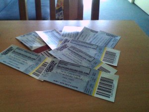 a pile of tickets to comedy festival shows on top of a pine table surface