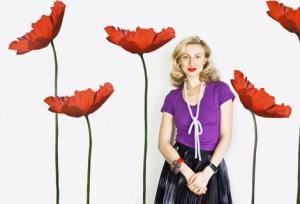 Poppy King in purple top and black skirt, surrounded by giant poppies.