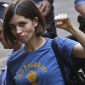 Tolokonnikova, wearing a blue t-shirt with a political slogan, raises a fist, while leaving court..