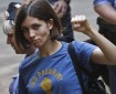 Tolokonnikova, wearing a blue t-shirt with a political slogan, raises a fist, while leaving court..