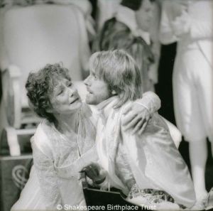 Black and white photo of a distressed man and woman in Regency costume, seated on the ground.