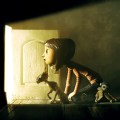Still from the movie showing Coraline and the black cat peering into a small, lighted doorway.