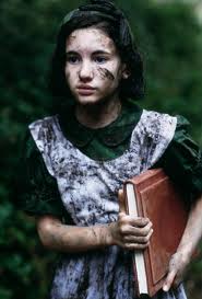 Girl of about 12 in a muddy pinafore, holding a large book.