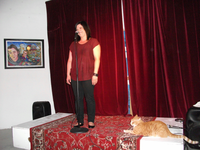 A large Ginger tabby cat lies on the stage staring at the performer (Rebecca de Unamuno)