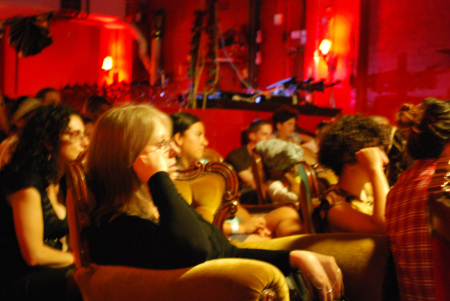 A group of mainly women sitting in comfy chairs watching something.