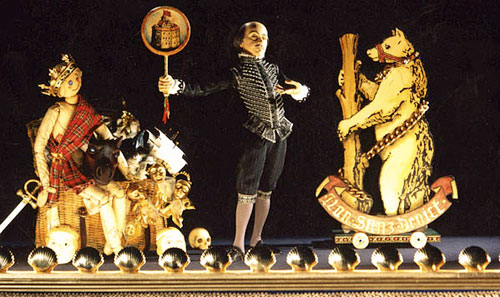 Puppet Shakespeare behind footlights, with a large basket full of props, and a cutout bear.