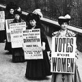 B&W photo of a row of Edwardian women holding signs demanding the vote.