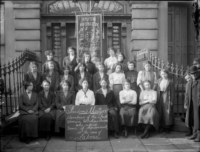 B&W group of 20-something Irish women in early 20th century with a banner saying "Irish Women Workers Union" & chalkboard reading "Freedom Martyrs".
