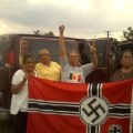 Four elderly but strong looking indigenous American women stand next to a van. They are holding a captured Nazi flag and cheering in preparation for burning it.