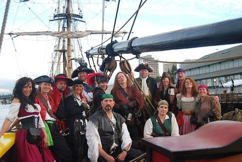 Group of men and women dressed as pirates in front of a tall ship.