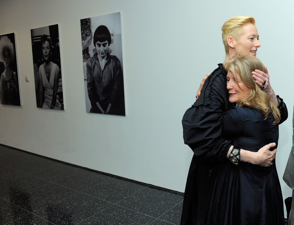 Tilda Swinton embraces the much shorter Sally Potter, in front of large photo portraits.