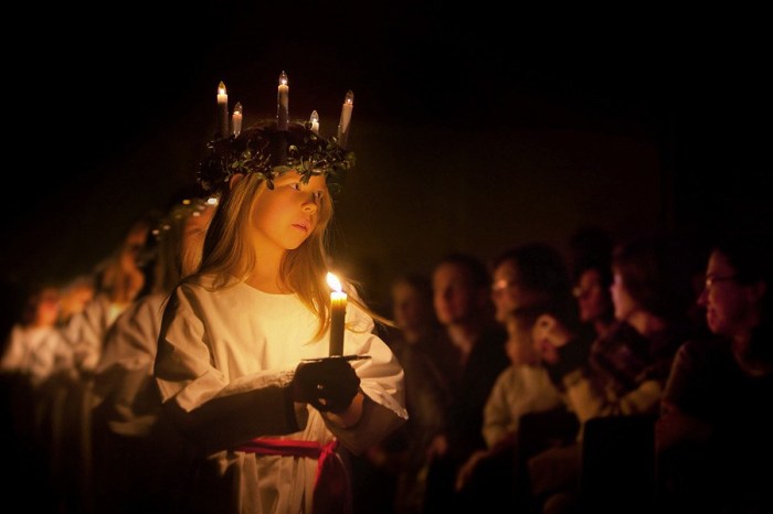 Young blonde girl wearing candle crown and carrying candle, with others behind her.