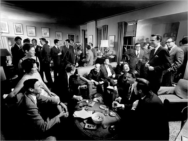 B&W large room full of people in casual evening dress, 1960s style.