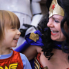 Woman in Wonder Woman costume laughs with child in WW shirt.