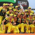 A group of jubilant sportswomen in the Australian national colours of green and gold pose for a photo with a championship trophy