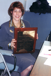 Dr Brodsky seated, holding a plaque.