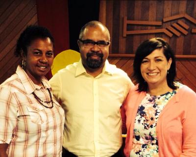 Two Aboriginal women either side of Aboriginal man, smiling to camera.