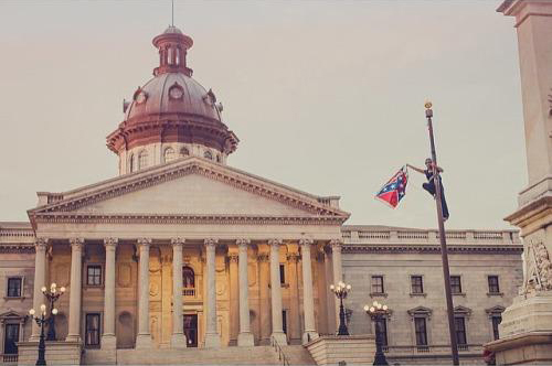 Capitol building with woman halfway up the flagpole, holding flag.