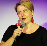 Middle aged white woman speaking into hand-held microphone.