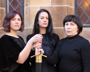 Three brunette women of varying ages grasping a sword hilt.